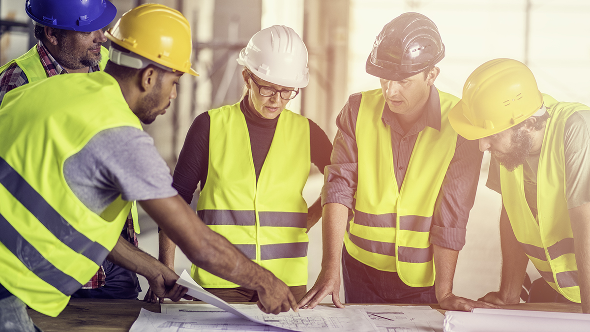 Construction engineer consulting female architect, construction foreman and construction workers about blueprints.